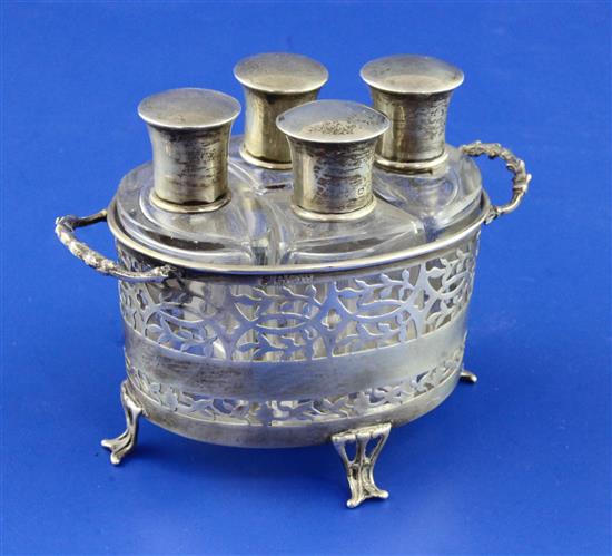 A George V pierced silver two handled scent bottle stand containing four silver mounted shaped glass scent bottles,